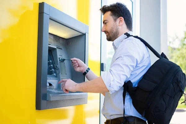 Egy férfi bankautomatánál intézi az ügyét, miközben a pénzfelvétel vagy készpénzellenőrzés folyamatában van.